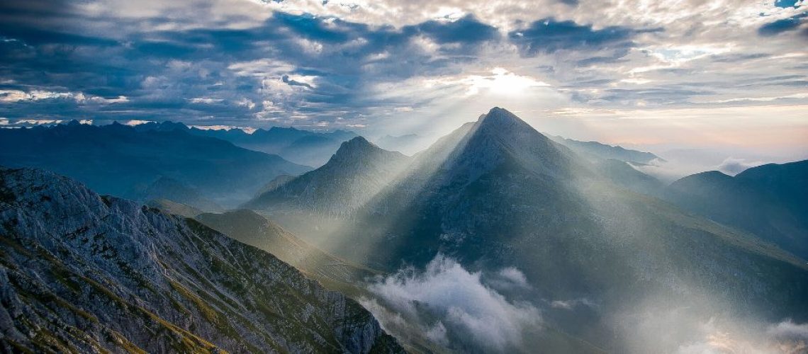 Image of sun rays shining onto mountain through clouds