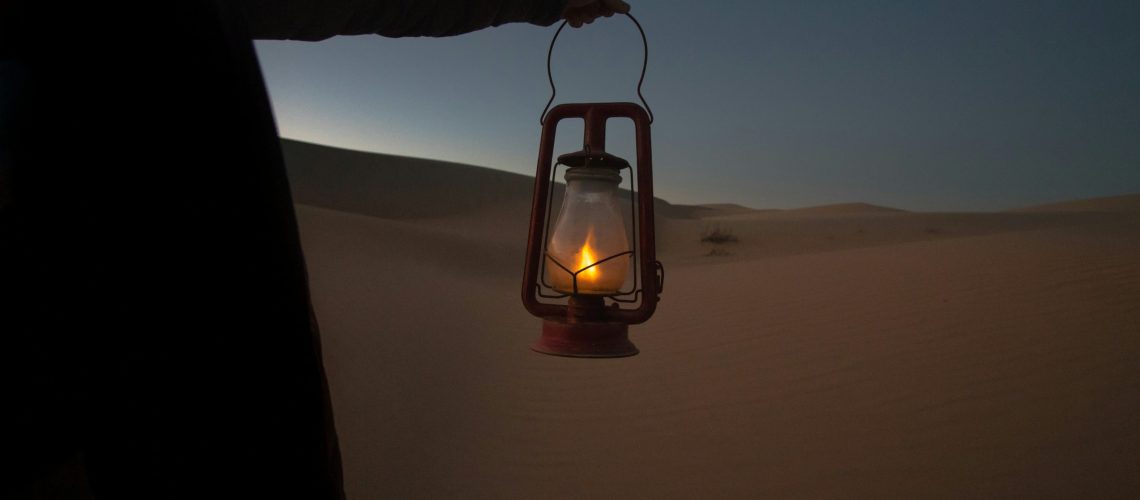 A person holding a lantern in the desert at dusk, symbolizing guidance and sincerity in daily actions